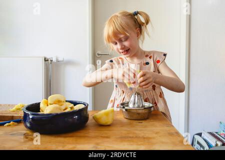 Fille pressant le citron à l'aide de presse-agrumes à la maison Banque D'Images