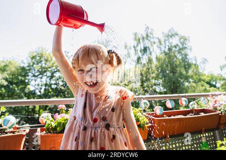 Fille souriante versant de l'eau sur la tête dans le balcon Banque D'Images