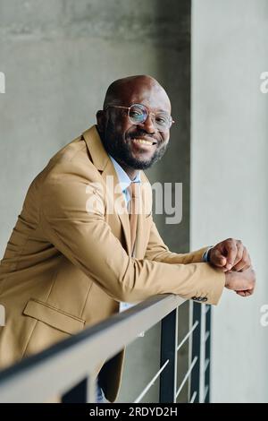 Homme d'affaires souriant en costume appuyé sur la rampe Banque D'Images