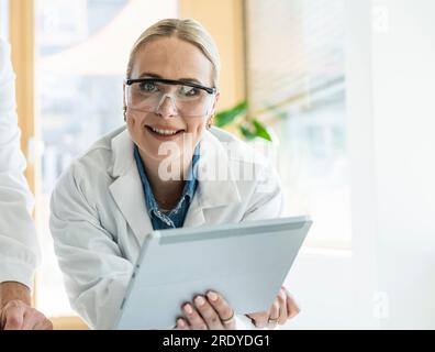 Scientifique souriant portant une blouse de laboratoire tenant la tablette PC dans le laboratoire Banque D'Images