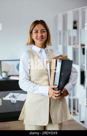 Femme d'affaires souriante avec des dossiers dans le bureau Banque D'Images