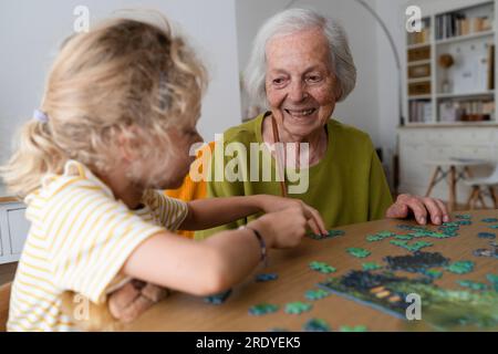 Grand-mère souriante regardant sa petite-fille résoudre le puzzle Banque D'Images