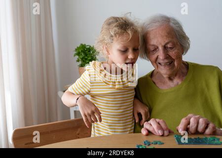 Grand-mère enseignant petite-fille pour résoudre puzzle à la maison Banque D'Images