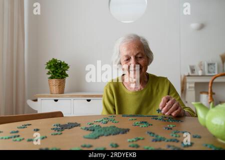 Femme senior résolvant puzzle à la maison Banque D'Images