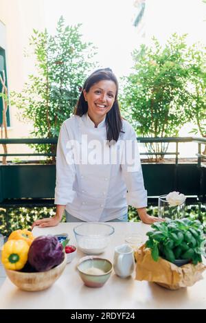 Chef souriant appuyé sur la table avec des ingrédients Banque D'Images