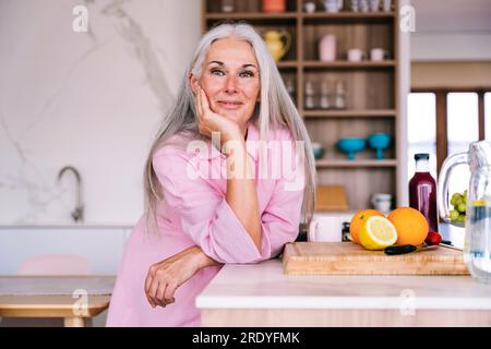 Femme souriante s'appuyant sur le comptoir de la cuisine à la maison Banque D'Images
