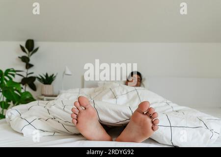 Jeune homme pieds nus reposant sur le lit à la maison Banque D'Images