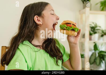 Fille heureuse mangeant Burger à la maison Banque D'Images