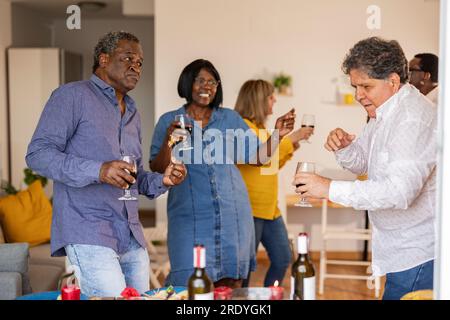 Heureux amis seniors multiculturels dansant ensemble au dîner Banque D'Images