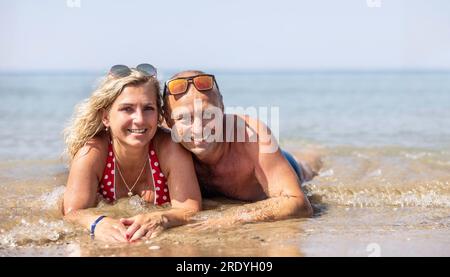 Un couple d'âge moyen allongé sur une plage au bord de la mer pendant une chaude journée d'été ; passer des vacances ensemble. Banque D'Images