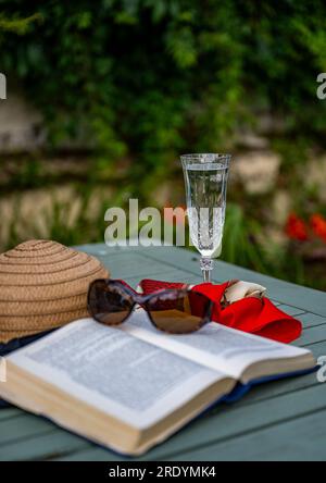 Scène emblématique d'été d'une chaude journée paresseuse d'été - un chapeau de soleil, un livre, une coupe de champagne et des lunettes de soleil Banque D'Images