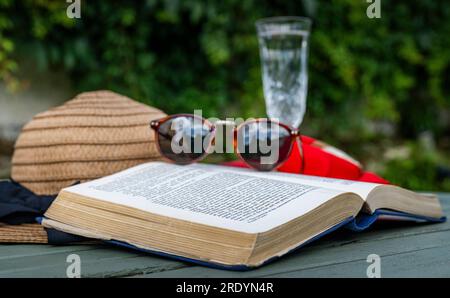 Scène emblématique d'été d'une chaude journée paresseuse d'été - un chapeau de soleil, un livre, une coupe de champagne et des lunettes de soleil Banque D'Images