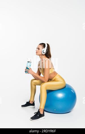 mode de vie sain, aérobic, femme en tenue active et écouteurs sans fil assis sur le ballon de fitness Banque D'Images