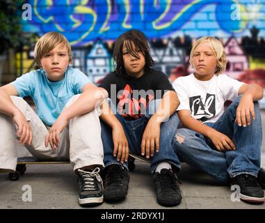 Portrait de trois garçons assis sur leurs planches à roulettes devant un mur couvert de graffitis à San Francisco, Californie. Banque D'Images