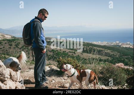 Homme souriant au chien dans les montagnes à Malaga contre le ciel bleu et l'océan Banque D'Images