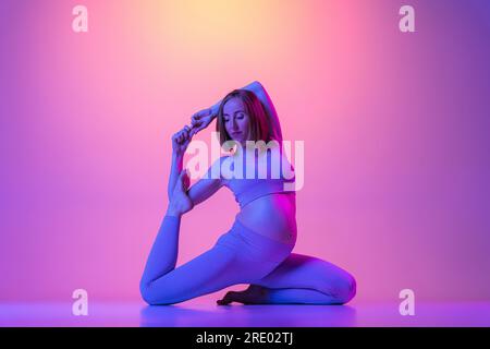 Femme enceinte faisant des jambes étirant des exercices de yoga au néon Banque D'Images