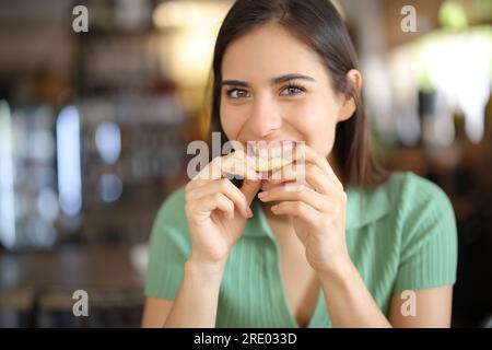 Portrait vue de face d'une femme heureuse dans un bar mordant le citron Banque D'Images