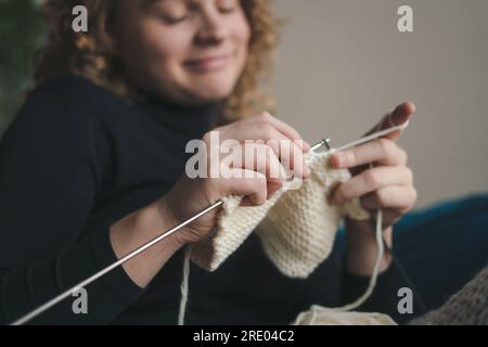 Vue rapprochée des mains d'une femme tricotant dans une lumière confortable. Crocheter des fils épais. Confort à la maison. Banque D'Images