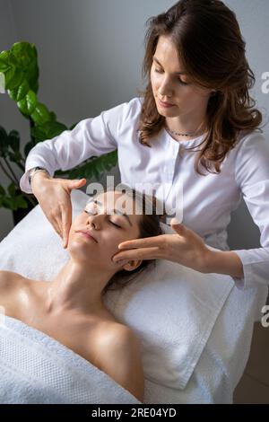 Thérapeute professionnel faisant la procédure de lifting de peau à la femelle mature détendue couchée sur la table dans le salon de spa. Traitement relaxant en médecine Banque D'Images