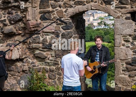 St Anthony's Chapel Holyrood Park, Édimbourg, Écosse, Royaume-Uni, 24 juillet 2023. Clip de Mike Baillie pour Fringe show : le chanteur du groupe The Lonely Together filme un nouveau clip pour son premier show Fringe Endless Sunset Oblivion qui raconte l'histoire d'un jeune compositeur Reuben qui tente de combattre les problèmes accélérés auxquels le monde est confronté. La chanson dans la vidéo a été écrite à cet endroit. Crédit : Sally Anderson/Alamy Live News Banque D'Images