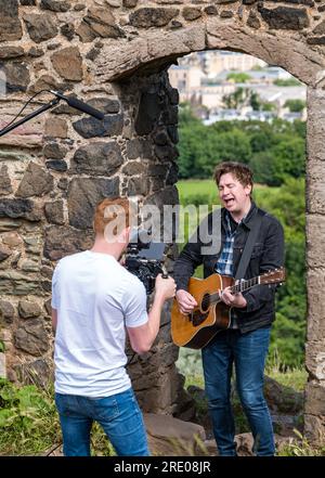 St Anthony's Chapel Holyrood Park, Édimbourg, Écosse, Royaume-Uni, 24 juillet 2023. Clip de Mike Baillie pour Fringe show : le chanteur du groupe The Lonely Together filme un nouveau clip pour son premier show Fringe Endless Sunset Oblivion qui raconte l'histoire d'un jeune compositeur Reuben qui tente de combattre les problèmes accélérés auxquels le monde est confronté. La chanson dans la vidéo a été écrite à cet endroit. Crédit : Sally Anderson/Alamy Live News Banque D'Images