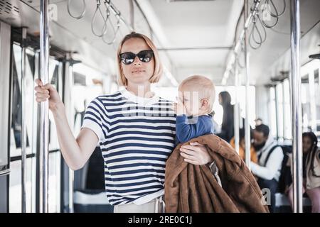 Mère porte son enfant tout en se tenant debout et tenant sur le porte-barre dans le bus. Maman tenant bébé garçon dans ses bras tout en roulant dans les transports en commun. Mignon enfant voyageant avec la mère Banque D'Images