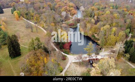 Magnifique vue sur un parc d'automne avec des arbres avec des feuilles mortes jaunes, des lacs, de l'architecture, des clairières et des personnes marchant le long des chemins de terre le jour de l'automne. Vol au-dessus du parc d'automne. Vue de dessus. Banque D'Images