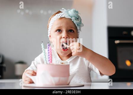 Adorable enfant de trois ans célébrant son anniversaire et soufflant des bougies sur un gâteau cuit maison, à l'intérieur. Banque D'Images