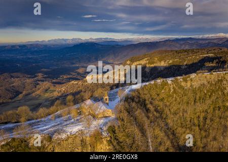 Vue aérienne des falaises de Cabrera et du sanctuaire lors d'un lever de soleil hivernal avec neige à Collsacabra (Osona, Barcelone, Catalogne, Espagne) Banque D'Images