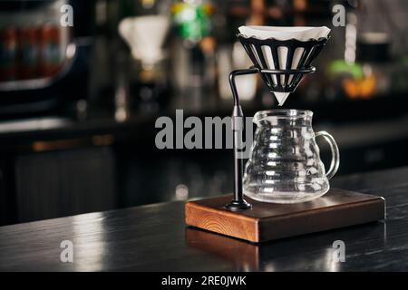 Méthode de style V-60, support goutteur avec sac filtrant au-dessus d'une cafetière en verre sur un comptoir en bois noir Banque D'Images