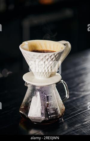 Goutteur en céramique avec café versé sur pot en verre dans le café sur la table noire, style alternatif V-60 Banque D'Images