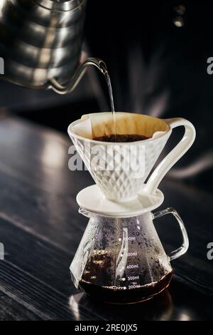 Infusion alternative d'espresso de style V-60, eau bouillante versée dans le goutteur en céramique placé sur le pot en verre Banque D'Images