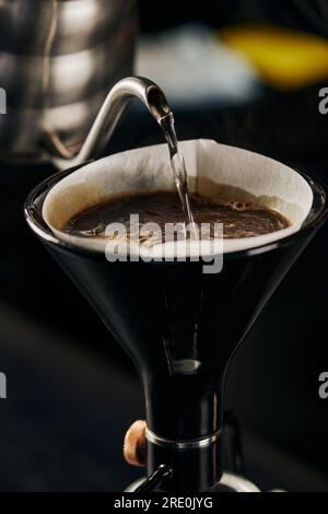 eau bouillante versant de la bouilloire dans la cafetière siphon avec filtre en papier et café avec mousse Banque D'Images