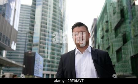 Un jeune homme d'affaires prospère dans un costume gris strict se promène dans la ville. Un homme heureux en costume se promène dans la ville et sourit. Un et joyeux Banque D'Images