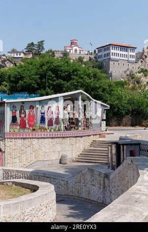 Plovdiv, Bulgarie. Entrée du métro et boutique avec illustrations de vêtements traditionnels. Église en arrière-plan sur la colline. Banque D'Images