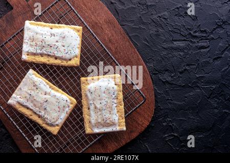 Déposer les tartes sur une grille de cuisson. Poptart grille-pain pâtisserie avec glaçage sur un fond noir, plan de pose plat au-dessus de la tête avec espace de copie Banque D'Images