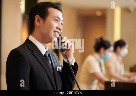 Le directeur de l'hôtel spa vietnamien parle au téléphone avec le client qui commande le petit déjeuner dans la chambre Banque D'Images