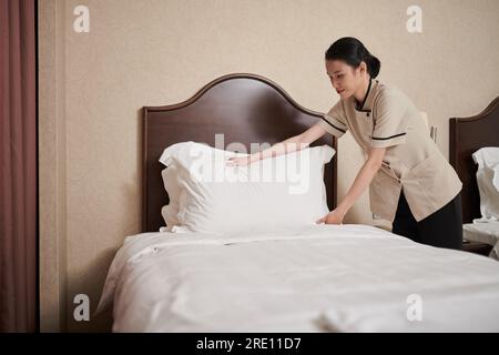 Souriante jeune femme de ménage asiatique changeant le linge et faisant le lit Banque D'Images