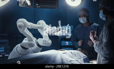 Deux chirurgiens observant des bras robotiques automatisés programmables de haute précision opérant un patient dans un hôpital de haute technologie. Membres robotisés pratiquant la chirurgie Banque D'Images
