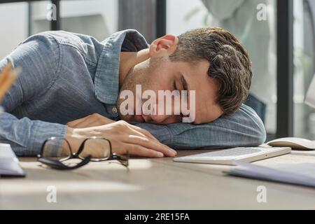 Homme d'affaires fatigué dormant sur son bureau devant l'ordinateur portable, surtravaillant, se sentant épuisé dans le bureau moderne. Banque D'Images