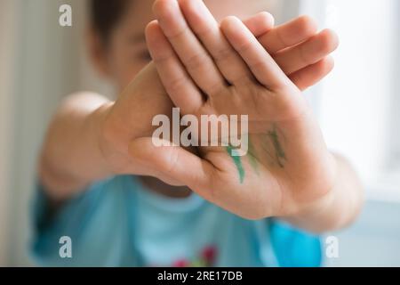 Garçon cachant son visage et montrant ses mains après avoir fait des activités de peinture. Concept d'apprentissage, compétences, enfance heureuse. Concentrez-vous sur les mains. Banque D'Images