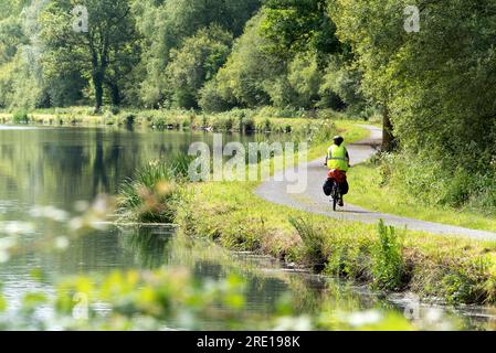 Cycliste vue de derrière sur un chemin de halage le long de la rivière Blavet, femme avec une veste jaune faisant du vélo. Vacances et balade à vélo en Languidic ( Banque D'Images