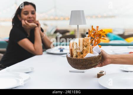 Serveuse servant une tranche de pain hors-d'œuvre sur la table pour le dîner avec le client en arrière-plan. Banque D'Images