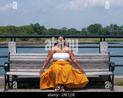 Femme afro-américaine Chubby dehors assise sur un banc Banque D'Images