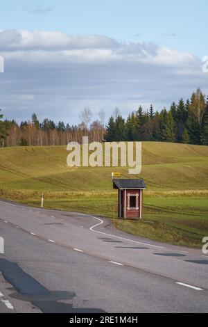 Arrêt de bus dans la campagne finlandaise avec abri en bois rouge et champs verts en arrière-plan Banque D'Images