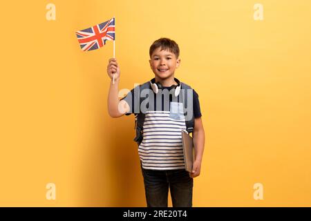 Garçon d'école mignon montrant drapeau du Royaume-Uni, fond jaune Banque D'Images