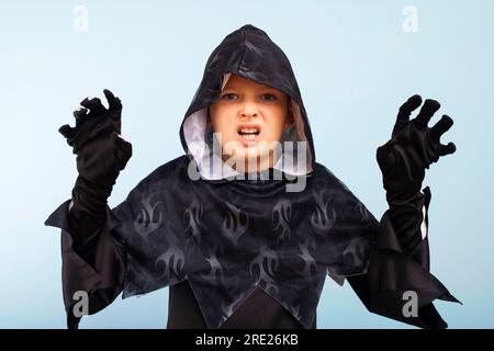 Portrait d'un petit garçon en colère dans un costume de sorcier sur un fond bleu Banque D'Images