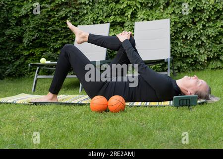 Femme blonde en survêtement noir sur l'herbe faisant de la gymnastique à la maison dans le jardin Banque D'Images