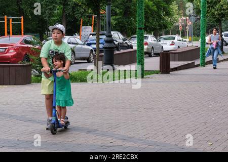 Kazakhstan, Almaty. Garçon et petite sœur sur Scooter sur la promenade Panfilov, une promenade piétonne. Banque D'Images