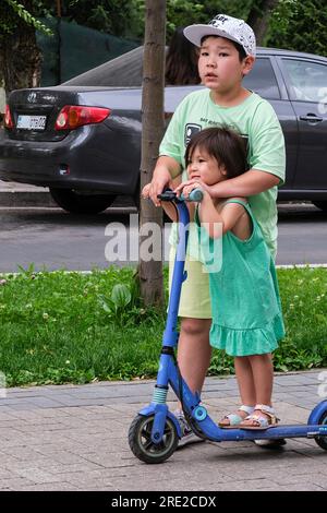 Kazakhstan, Almaty. Garçon et petite sœur sur Scooter sur la promenade Panfilov, une promenade piétonne. Banque D'Images